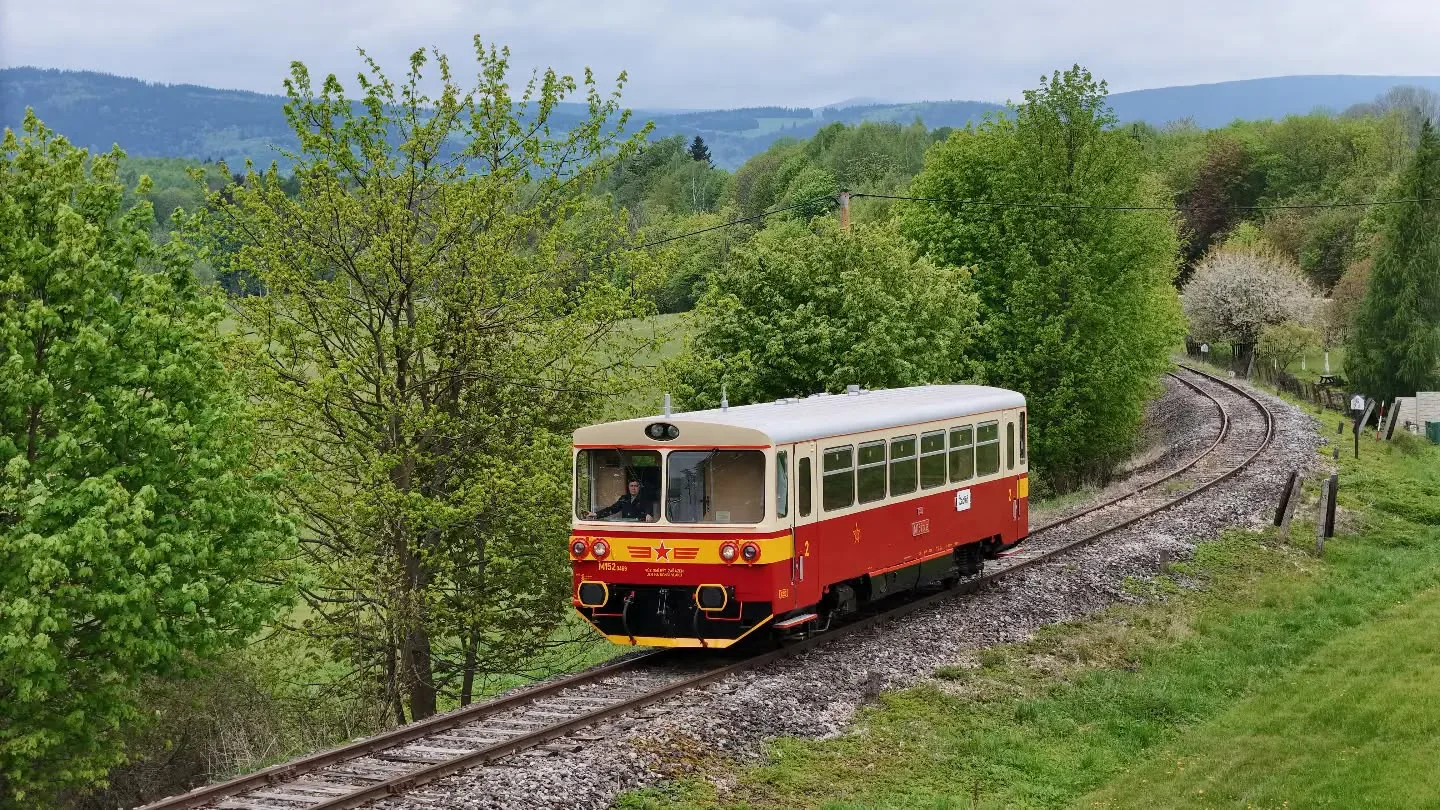 Červenobílý historický motorový vůz M 152 projíždí obloukem v zelené krajině.