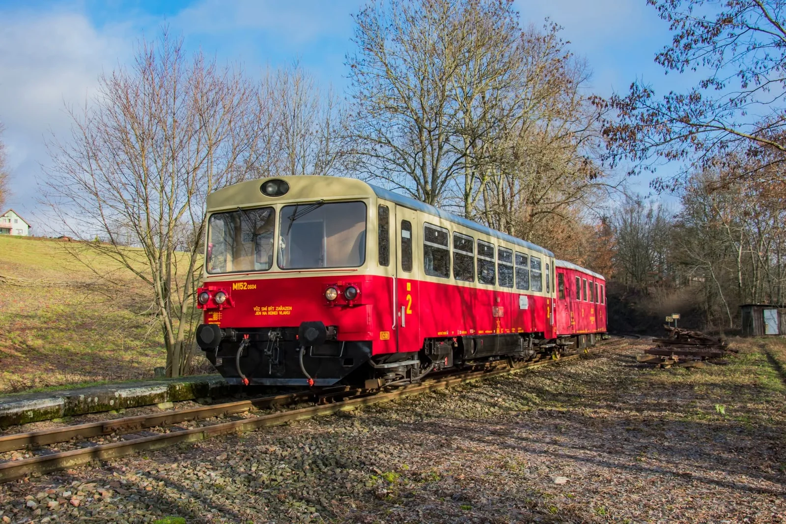 Červenobílý motorový vůz M 152 s přípojným vozem projíždí zimní krajinou.